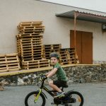 Young boy with helmet riding a bicycle outside an industrial building.
