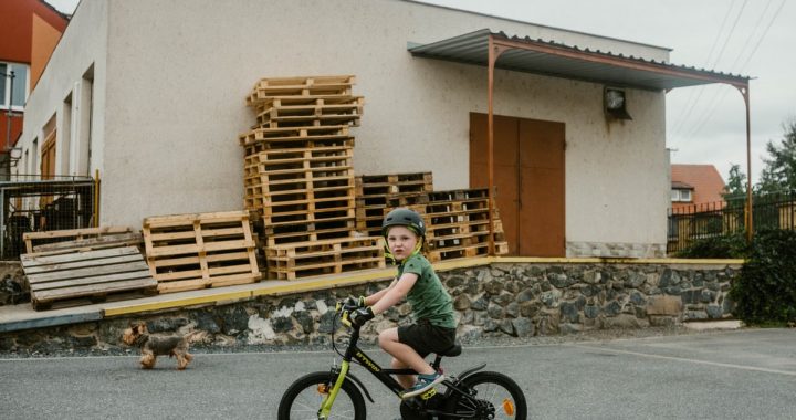 Young boy with helmet riding a bicycle outside an industrial building.